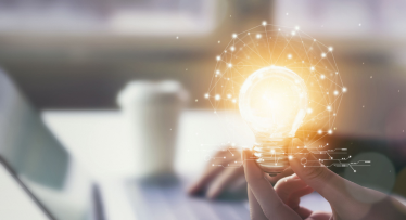 Osoba pracująca na komputerze trzyma w ręku żarówkę