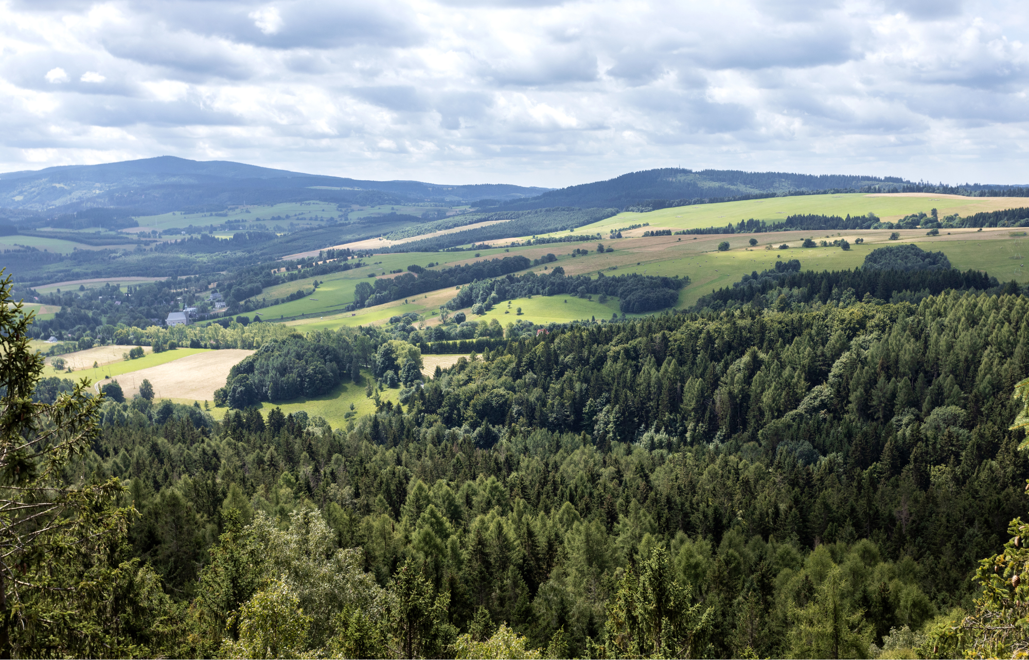 Zdjęcie przedstawia pejzaż gór i łąk i niewielkie miasteczko w oddali