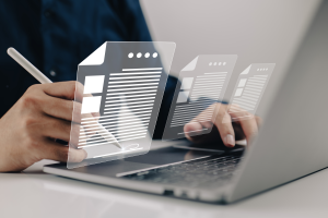 Klawiatura laptopa, nad którą wyświetlają się interaktywne grafiki symbolizujące dokumenty.
