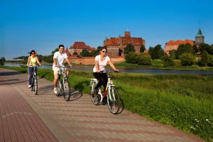 trzy osoby jadą ścieżką rowerową. W tle zamek w Malborku