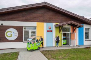 Zdjęcie budynku, w którym działa klub dziecięcy "GórzMisie" w Górznie. Dzieci wyjeżdżają na spacer w  kolorowych jeździkach (autkach) prowadzonych przez opiekunki. 